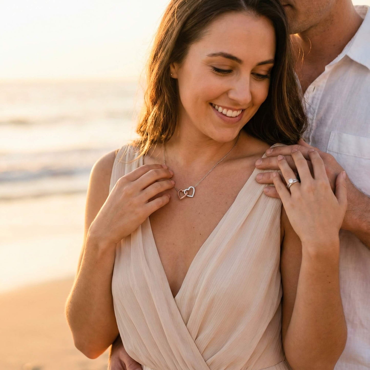 Happy couple embracing on the beach, wearing the meaningful interlocking hearts necklace gift.