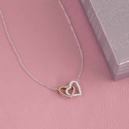 Necklace with interlocking hearts pendant on a pink surface