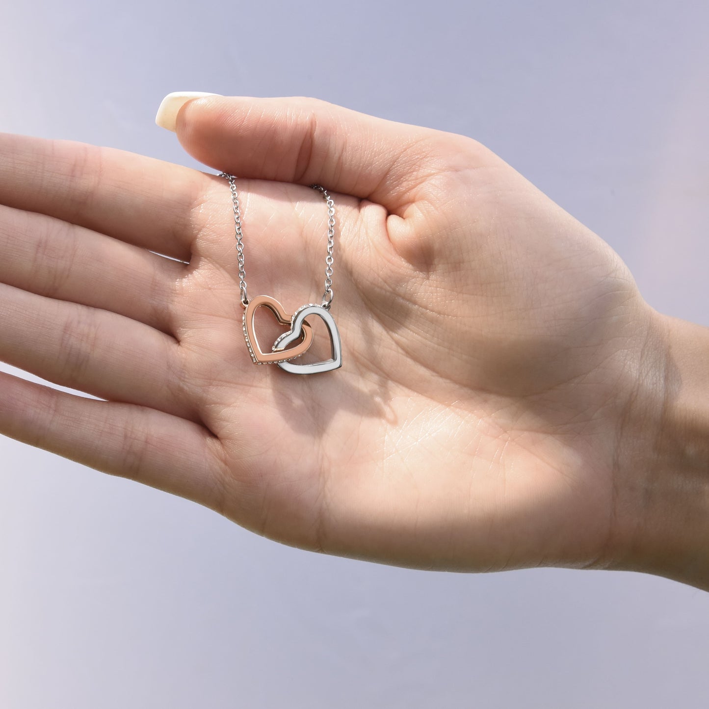 Hand holding a necklace with interlocking hearts pendant against a light background